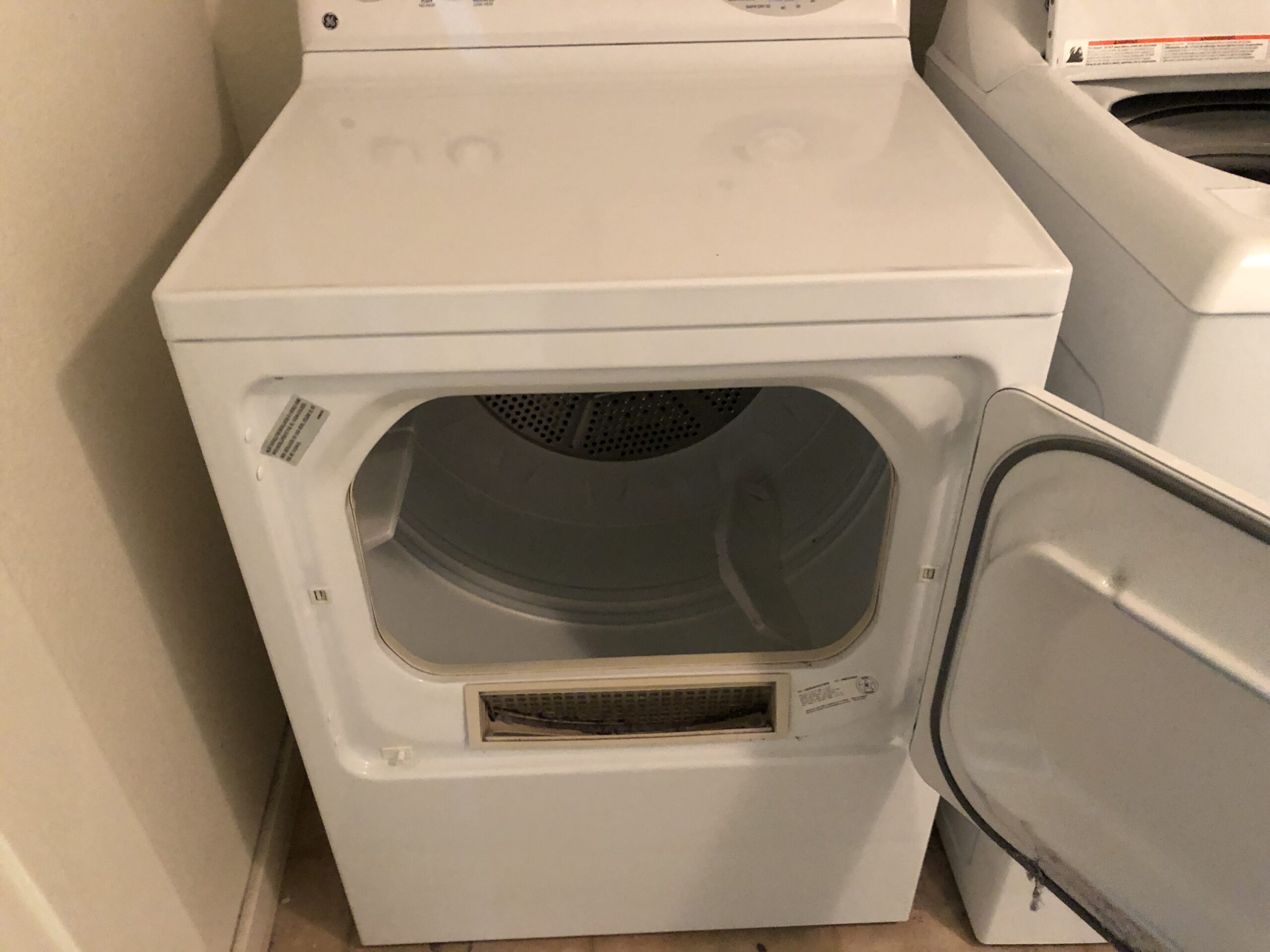 White clothes dryer with door open showing drum interior where model and serial number tag is located